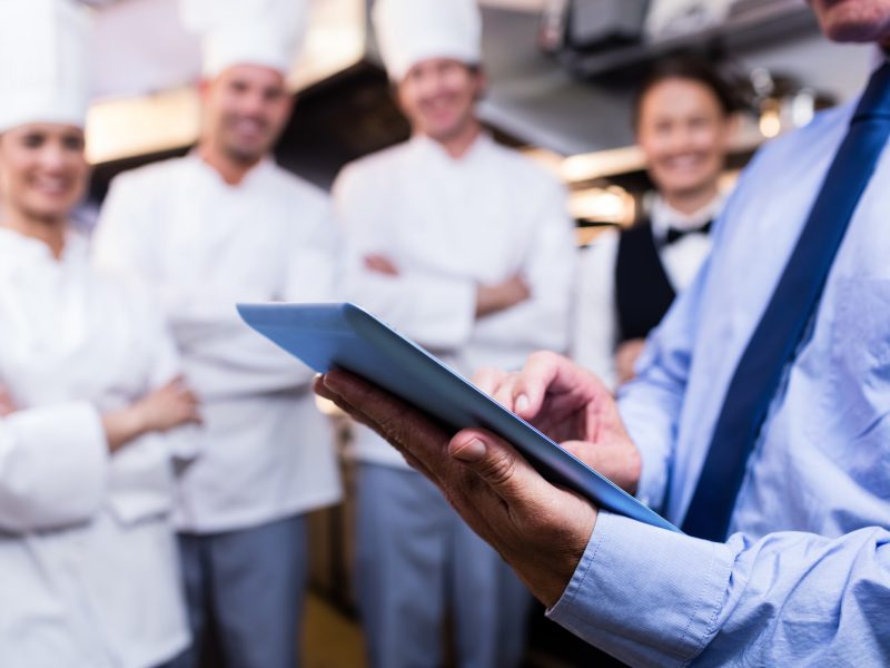 Mid section of restaurant manager using digital tablet in commercial kitchen